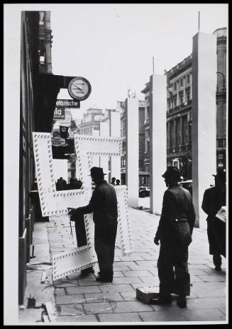 A man manoeuvring a large Swastika sign, in the street.