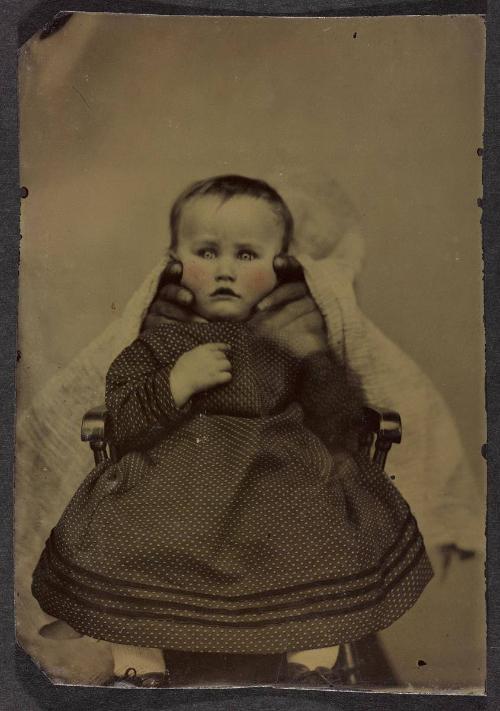 Portrait of young child in polka-dot dress (seated on chair with hands supporting face)