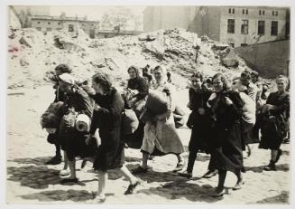 Group of women with sacks and pails, walking past synagogue ruins heading for deportation