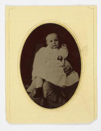 Portrait of baby wearing white dress and boots ( supported on lap of figure)