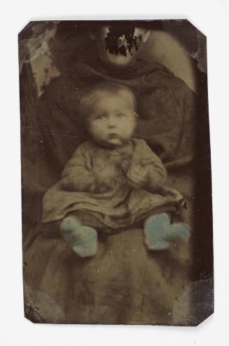 Portrait of baby wearing blue socks (seated on chair supported by defaced figure)