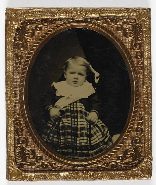 Portrait of young boy in plaid dress (seated on lap of defaced figure)