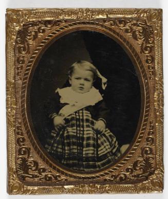 Portrait of young boy in plaid dress (seated on lap of defaced figure)
