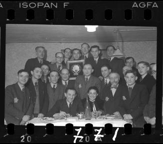 Group portrait of residents at a reception in the ghetto; man holding a framed award in the centre