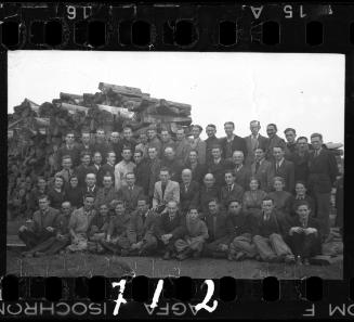 Large group portrait of members of the ghetto administration beside a pile of lumber