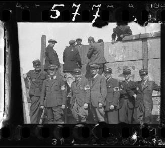 Six Jewish police and an administrator standing in front of workers building a wall