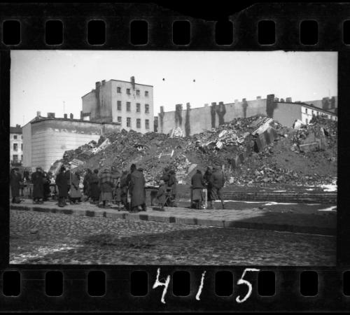 Small group of residents standing on the street next to the ruins of the synagogue on Wolborska Street, destroyed by the Germans in 1939