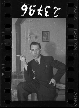 Man posing with a cigarette in front of a portrait of Mordechai Chaim Rumkowksi