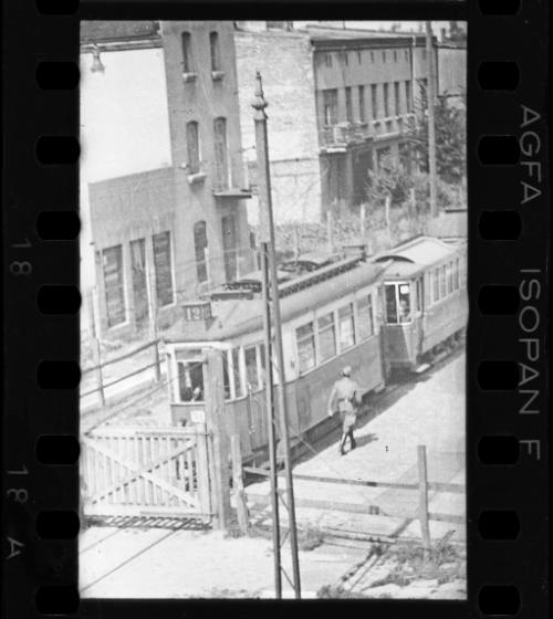 A German official walking beside tram, outside an entry gate to the ghetto