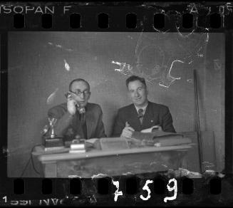 Transport Department administrator, Mr. Elefant (left), talking on the phone beside member of the ghetto administration