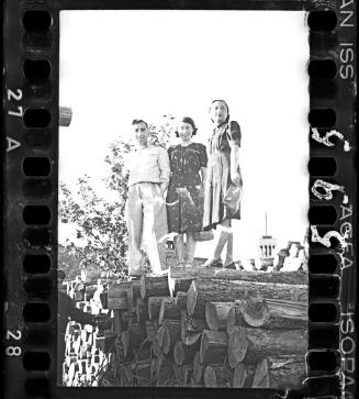 Two young girls and a man on top of a pile of timbers