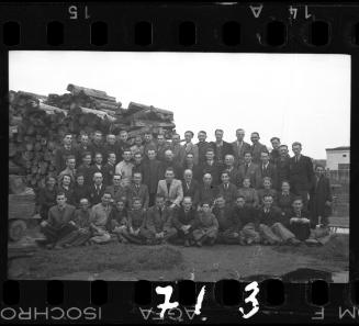 Large group portrait of members of the ghetto administration beside a pile of lumber
