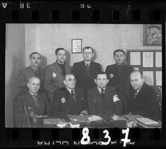 Group portrait of a Jewish police officer and members of the ghetto administration in an office