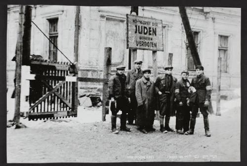Six men pose outside of restricted ghetto area underneath 'JUDEN' sign