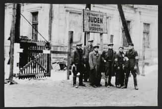 Six men pose outside of restricted ghetto area underneath 'JUDEN' sign