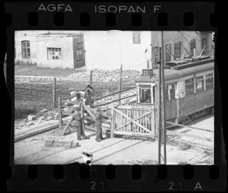 Two Jewish policemen guarding an entry gate to the ghetto, with a streetcar approaching the gate