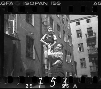 Man holding child in the air, outside of ghetto buildings