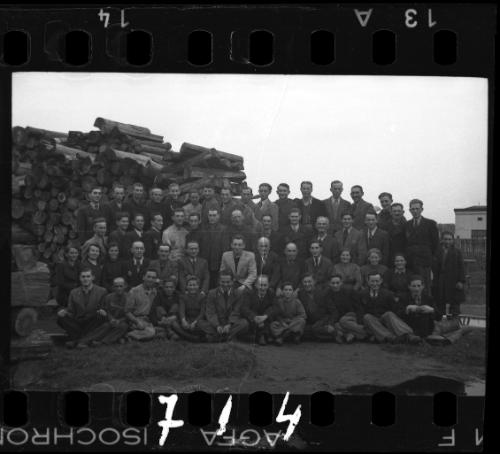 Large group portrait of members of the ghetto administration beside a pile of lumber