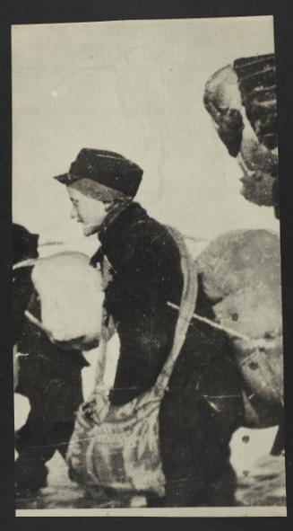 Boy in cap, with satchel and sack tied to back, walking with deportation crowd - side-profile
