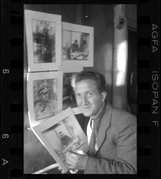 Mendel Grossman posing with portraits of German officers and administrators