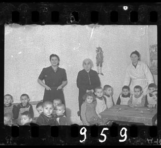 Childcare staff and children sitting around a table [probably in the orphanage]