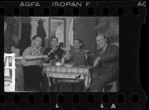 Four men sitting around a table, raising their drinks in celebration