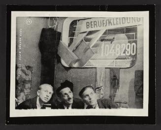 Henryk Ross with two men in front of "Berufskleidung" ['Workwear'] sign
