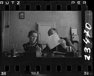 A man and woman working in an office, with a portrait of Mordechai Chaim Rumkowksi on the wall