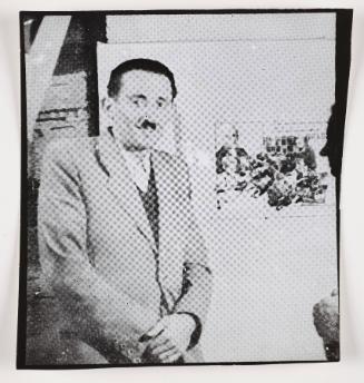 Henryk Ross standing beside photomontage promoting factory production in the ghetto
