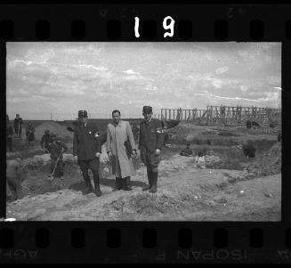 A German official and two Jewish policeman standing in front of workers digging trenches