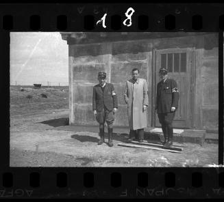 A German official and two Jewish policeman standing in front of a shack