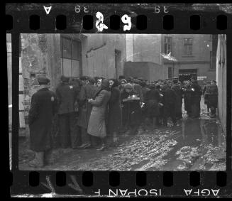 Residents carrying pails, line-up outside an unidentified building (probably a soup kitchen)