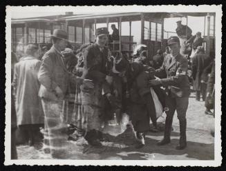 Two Jewish policemen holding elderly man in front of deportation tram