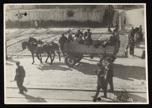 Three ghetto police walking on street along horse-drawn labour wagon