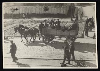 Three ghetto police walking on street along horse-drawn labour wagon