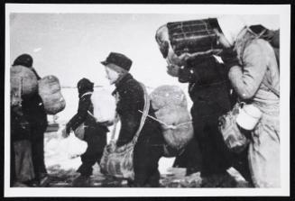 Boy in cap, with satchel and sack tied to back, walking with winter deportation crowd -side-profile