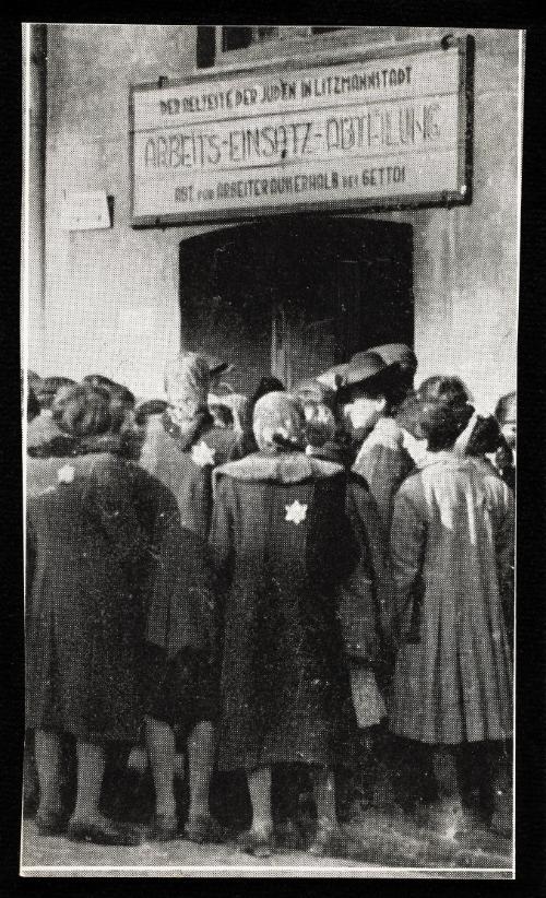 Ghetto residents gathered outside of doorway, under a Labour Department sign "ARBEITS-EINSATZ-ABTEILUNG, der aelteste der Juden in Litzmannstadt, abt. fur arbeiterausserhalb dei gettos"