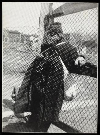 Man with bundles leaning against fence