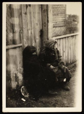 Two women wrapped in blankets, sitting on street