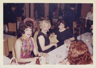 [Susanna in a pink, green and yellow dress, sitting with Anita and Gail, location unknown]
