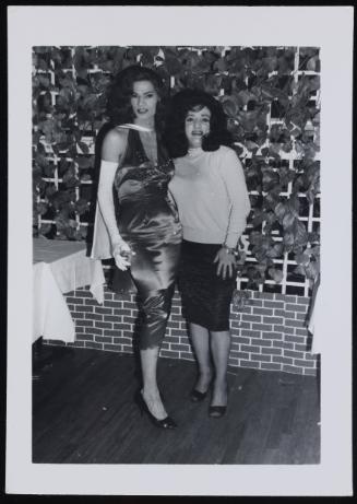 [Two brunettes in front of a vine-covered fence, location unknown]
